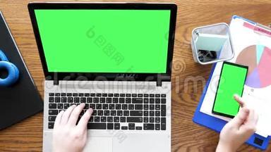 男人用手在带有绿色屏幕的笔记本电脑上打字，然后触摸智能手机上的绿色屏幕显示器